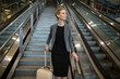 © Wavebreak Media - Female business traveler standing at base of granite staircase in airport hub holding suitcase