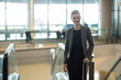 © Wavebreak Media - Businesswoman descending escalator holding handrail and rolling suitcase in terminal, copy space