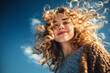 © Crowded Studio - Libertad y alegría, vibrando con la energía del buen tiempo.Mujer joven de cabello rizado sonríe feliz bajo un cielo azul vibrante.