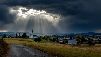Wall Mural - sunrays breaking through dark clouds, dramatically highlighting rural church standing among rolling 