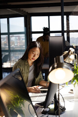 Asian woman coding on laptop in modern office, focused on work