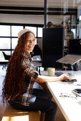 Smiling woman coding at desk with laptop and dual monitors in office