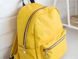 © rehena - Stylish yellow backpack or rucksack with zippers for school or travel, leaning on a white brick wall