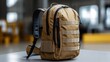 © Babb - A tactical backpack in a tan color is placed on a table inside a well-lit room. The design features multiple compartments and sturdy straps, showcasing its practical use
