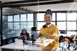 © Wavebreak Media - Holding tablet in office, confident woman smiling as colleagues collaborate on laptops