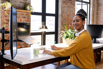 Smiling woman coding on laptop at office desk with headphones and coffee