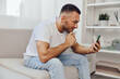 © SHOTPRIME STUDIO - Thoughtful man engaging with smartphone, exploring digital world, comfortable living room setting with modern decor, showcasing contemporary lifestyle.