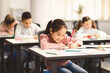 © Prostock-studio - Education And Studying Concept. Portrait of smiling asian small student sitting at desk in classroom, writing in notebook or drawing picture with colorful pencils. Back To School