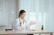 © Witoon - Young female doctor in lab coat and stethoscope working intently in front of laptop on desk in brightly lit office.