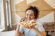 © Dusan Petkovic - Portrait of cheerful trendy interracial girl sitting in fast food restaurant with pizza in hand and talking on her phone