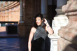 © Manuel - Portrait of young, beautiful, brunette woman, wearing a fancy black dress, looking at the camera, relaxed and calm, leaning on a marble column, receiving the sun's rays. Concept beauty, femininity.