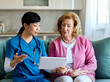 © Lumos sp - Doctor or nurse caregiver showing a tablet screen to  senior woman  at home or nursing home