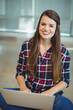 © WavebreakMediaMicro - Woman wearing plaid shirt sitting on carpet with laptop, smiling at camera in office lounge