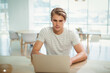 © WavebreakMediaMicro - Man sitting at wooden table in bright coworking lounge working on silver laptop with plastic chairs