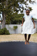 © wavebreak3 - African American girl bouncing on yard trampoline wearing tiara and fairy wings holding ribbon wand