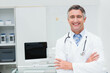 © WavebreakMediaMicro - Male doctor wearing lab coat, stethoscope crossing arms in office with computer monitor, copy space