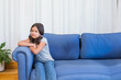 © WavebreakMediaMicro - Female child sitting on blue couch in living room with potted plant, white curtains, copy space
