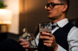 © aekachai - Businessman holding a glass of whiskey, sitting and drinking in a room