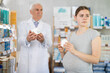 © caftor - Pregnant girl looking for skin cream in a pharmacy. Male pharmacist helps to choose right skin cream