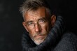 © Marina Varnava - Handsome senior man wearing glasses and a gray sweater poses warmly, showcasing his wise expression against a dark backdrop