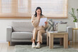© Pixel-Shot - Happy young woman with refund form sitting on sofa at home