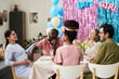 © pressmaster - Happy young couple expecting baby surrounded by diverse young adults celebrating gender reveal party with decorations