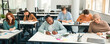 © Prostock-studio - Modern Education Concept. Portrait of diverse group of students sitting at desks in classroom at university, taking test, entrance examination or writing notes in notebook, selective focus