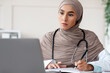 © Prostock-studio - Muslim female doctor having professional online training on laptop, taking notes while watching webinar, sitting at workdesk in clinic, copy space. Training for doctors, professional development