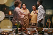 © Seventyfour - Group of Black family members gathering in living room for toast holding glasses at dinner party with food and drinks, while celebrating special occasion at home
