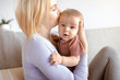 © Prostock-studio - Beautiful lady bonding with her adorable baby, holding cute sun or daughter and kissing, sitting on couch. Closeup portrait of loving mother young blonde woman kissing little kid, home interior