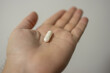 © HannaStudio - Hand holding single white capsule indicating medication or supplement usage.