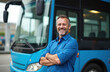 © Pete - Smiling bus driver with arms crossed stands proudly. Man in blue shirt poses near public transport bus. Concept of service job, people transportation, travel, occupation.