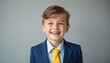 © Pete - Happy young boy in blue suit with yellow tie smiles at camera. Little kid in formal attire, confident look, good mood. Portrait, studio shot, grey background. Childhood dreams, future success concept.