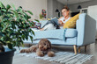 © Soloviova Liudmyla - Maltipoo dog lying on carpet napping after lunch while middle aged female reading book and relaxing on comfortable living room sofa enjoying quiet peaceful moment together in cozy home environment