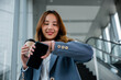 © sorapop - Businesswoman multitasking with smartwatch and smartphone while holding a cup of coffee. Modern office background. Perfect for technology and lifestyle themes.