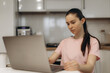 © Roman - Young Woman Focused on Work Using a Laptop in a Modern Kitchen