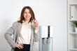 © Pixel-Shot - Smiling young woman drinking water from cooler in office