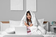 © Pixel-Shot - Morning of beautiful young woman with blanket using laptop in bedroom