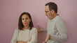 © Krakenimages.com - Middle-aged hispanic couple arguing against an isolated pink background depicting a tense family moment between a man and a woman expressing discontent.