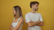 © Krakenimages.com - Man and woman standing back to back with crossed arms against a yellow background, representing conflict or disagreement in a relationship.