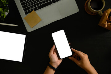 Wall Mural - hand holding smartphone with blank screen on dark desk workspace.