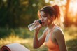 © HO - Athletic female with yoga mat sipping water, warm sunlight, green background