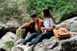 © itchaznong - Hiking Break. Young couple resting on rocks during a nature hike, enjoying each other's company.