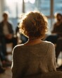 © Somporn - Woman with Curly Hair in Soft Lighting Engaged in Group Discussion During Therapy Session in Bright Room
