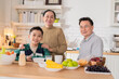 © whyframeshot - cheerful Asian family shares heartwarming moments as grandparents enjoy breakfast conversation with their grandson at home. The grandmother and young boy wash fresh fruits together in the open kitchen
