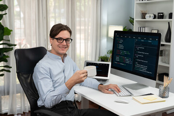 IT developer looking camera with holding coffee cup with online software on pc and laptop monitor beside, coding program on updated version application project creating new code system. Pecuniary.