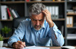 © starush - Frustrated middle-aged man with gray hair and beard working at desk in office