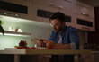 © My Ocean studio - Young man in glasses reading a small book at a kitchen counter, surrounded by notebooks, fruit, and a cup, appearing focused and engaged in a cozy, softly lit home environment.