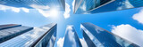 A worm's-eye view of tall, modern skyscrapers with glass facades reflecting the blue sky and clouds