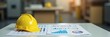 © Satou Akira - Yellow hard hat resting on top of business charts and graphs on a white desk in a blurred office or industrial setting